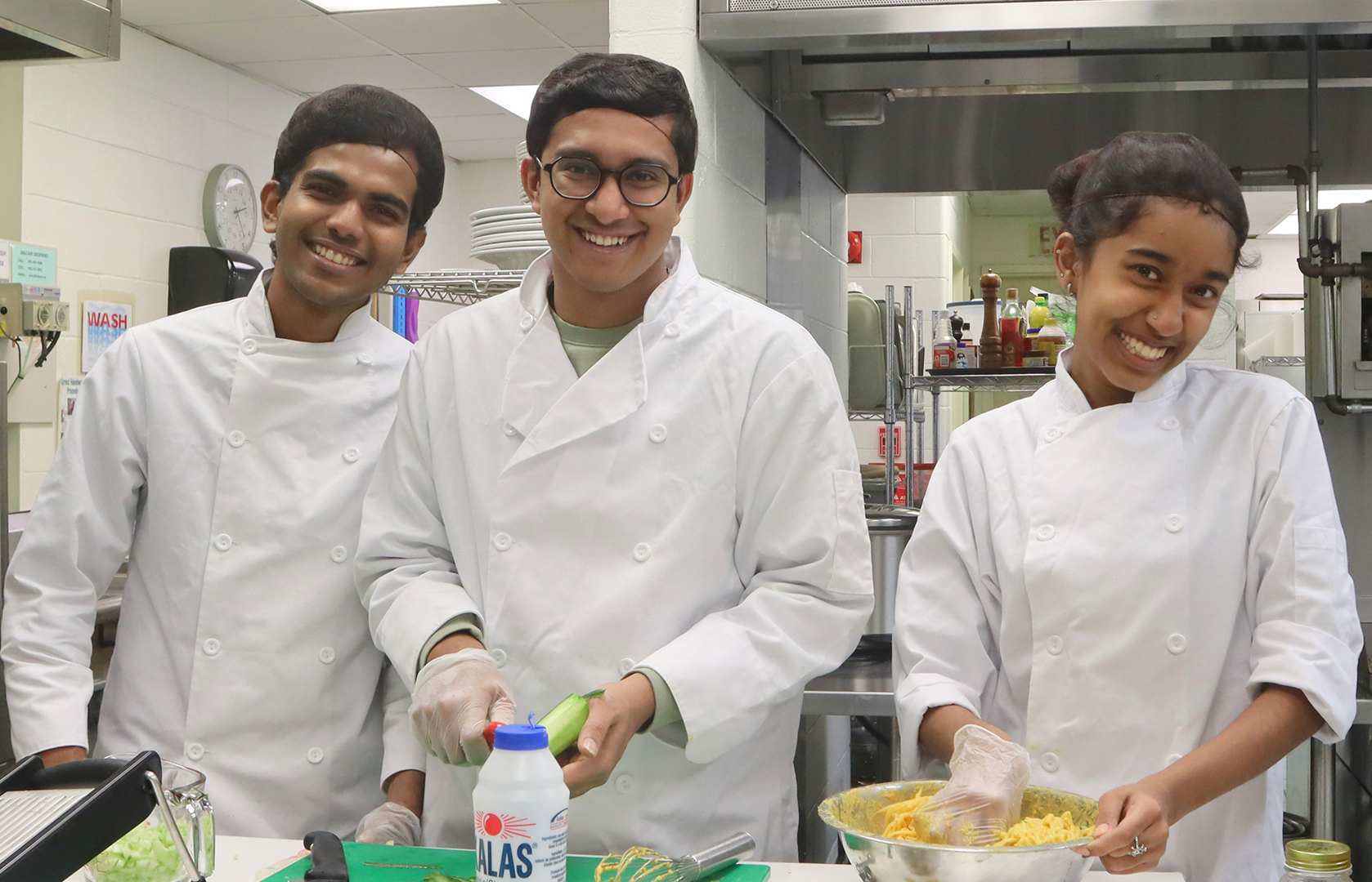 Three smiling Tourism and Hospitality students preparing food in Vincent's restaurant. 