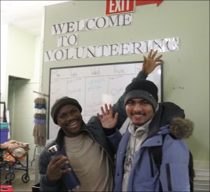 Two smiling guys at the Prescott Group standing under a sign that says welcome to volunteering during the business and tourism departments outing on Caritas Day 2025. 