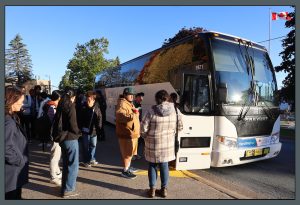 Students standing outside of Seton Academic Centre on a beautiful sunny day waiting to board the coach. 