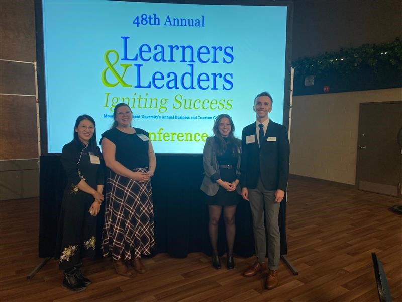 Business and Tourism society posing in front of the event sign at the Learners and Leaders conference 2022.