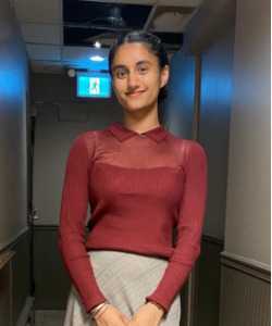 Picture of a woman in a redshirt and a grey skirt smiling into the camera