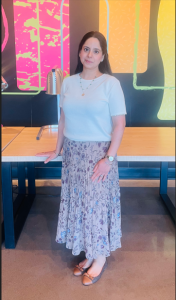 A picture of a woman standing in a blue shirt and a blue flurry skirt that reaches to her toes