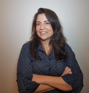 A headshot of Camila Alonso with arms folded at her chest in a blue spotted shirt