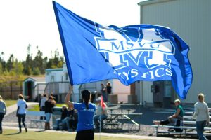 A student holding a MSVU Mystics flag on a field