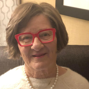 Ruby Blois, wearing red square frame glasses and a white sweater