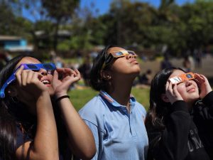 Three students wearing eclipse glasses looking at a solar eclipse