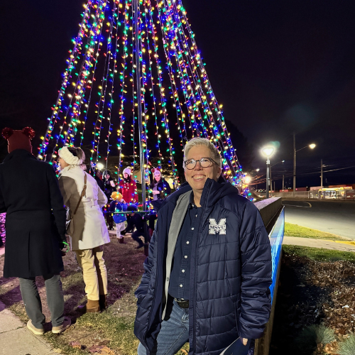 Dr. Joël Dickinson standing beside the tree for the Tree Lighting Ceremony event.