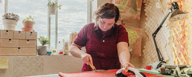 Melanie Colosimo, in a red shirt, measuring and cutting fabric